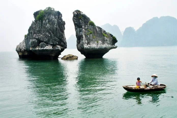 A small rowboat passes the twin rock formations known as Fighting Cocks Islets in Ha Long Bay.