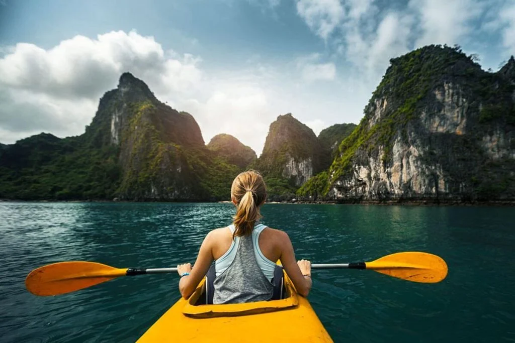 A paddler in a yellow kayak looks toward limestone cliffs across calm water.