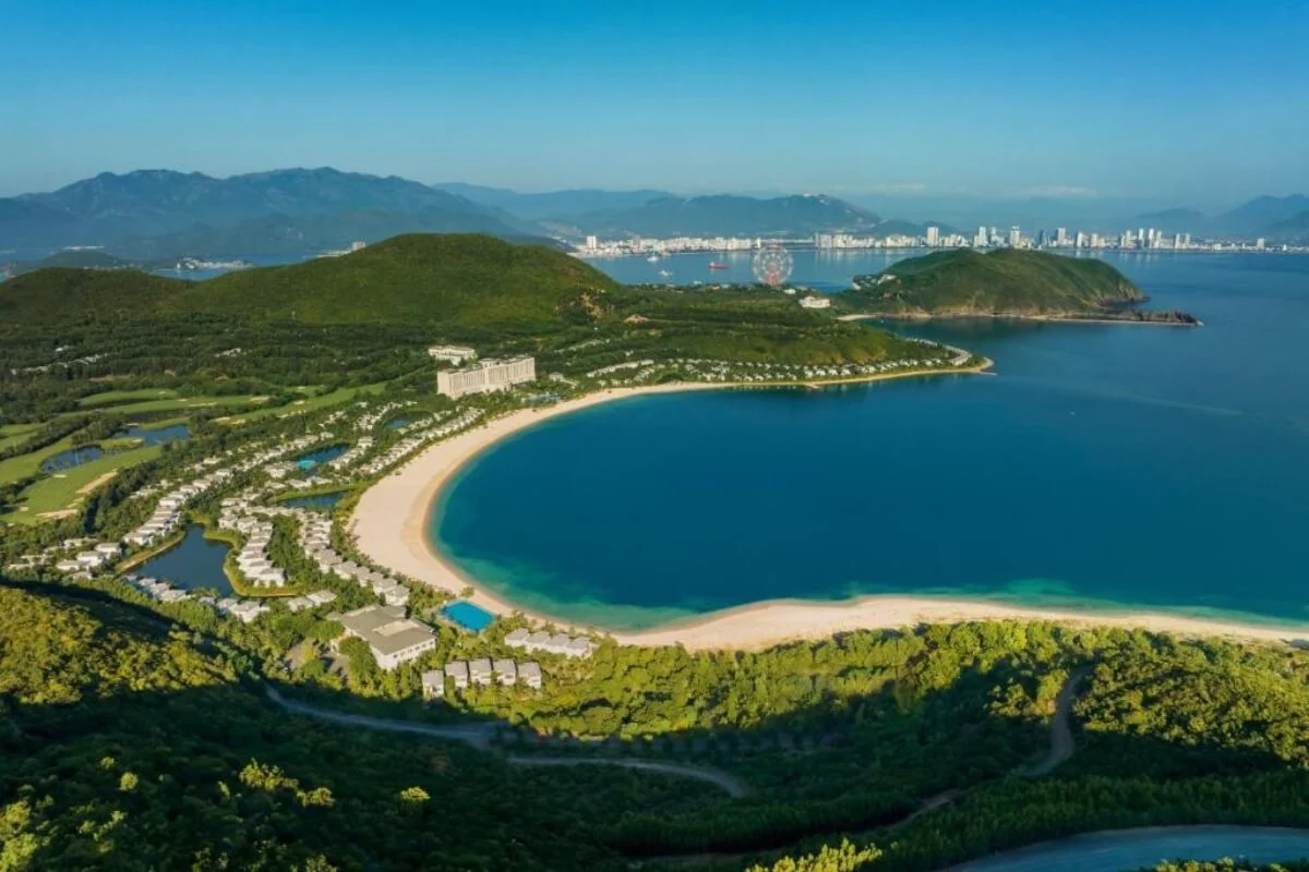 Resort villas and a crescent beach lie below green hills on Hon Tre Island.